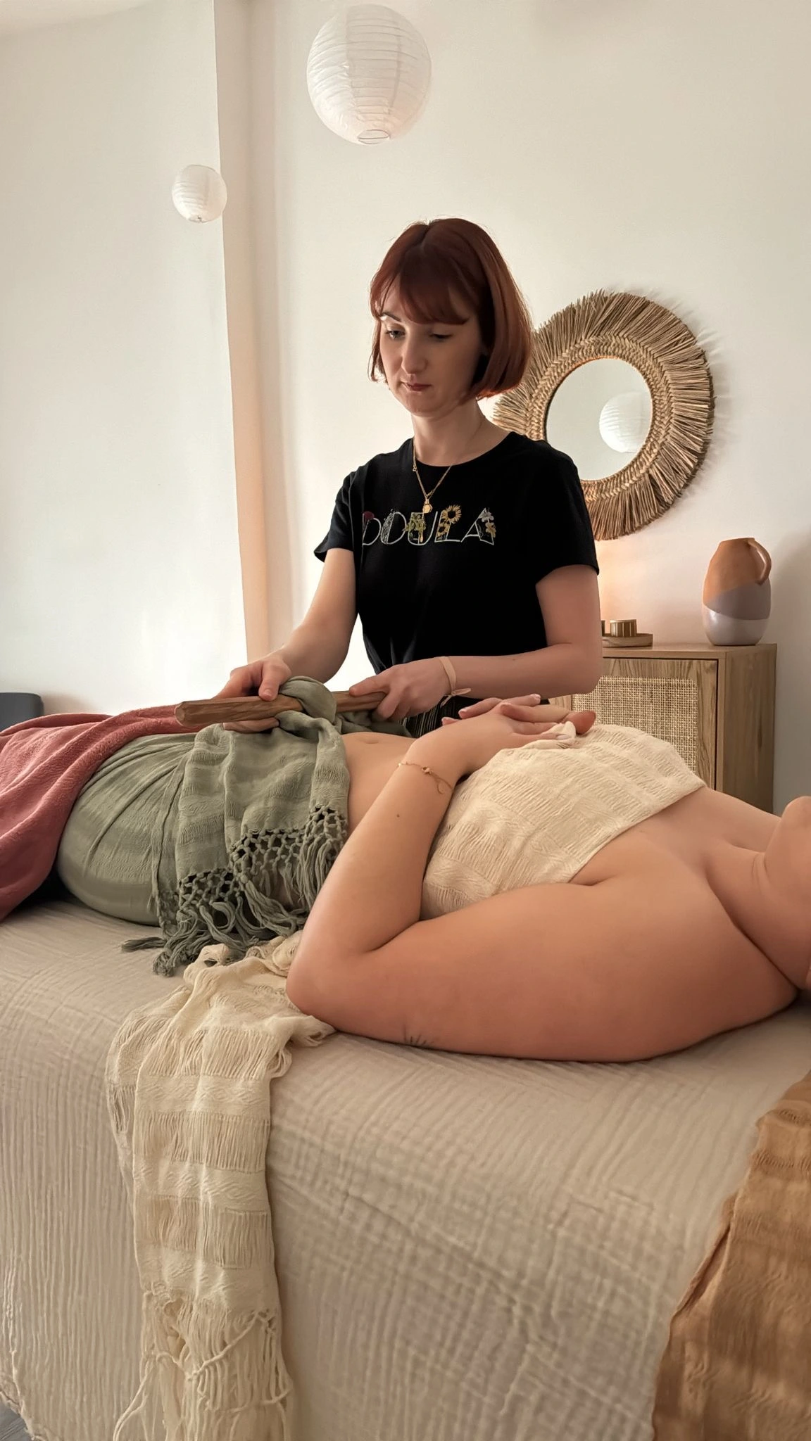 Doula tenant un bâton en bois pour effectuer un serrage sur le bassin d’une femme allongée