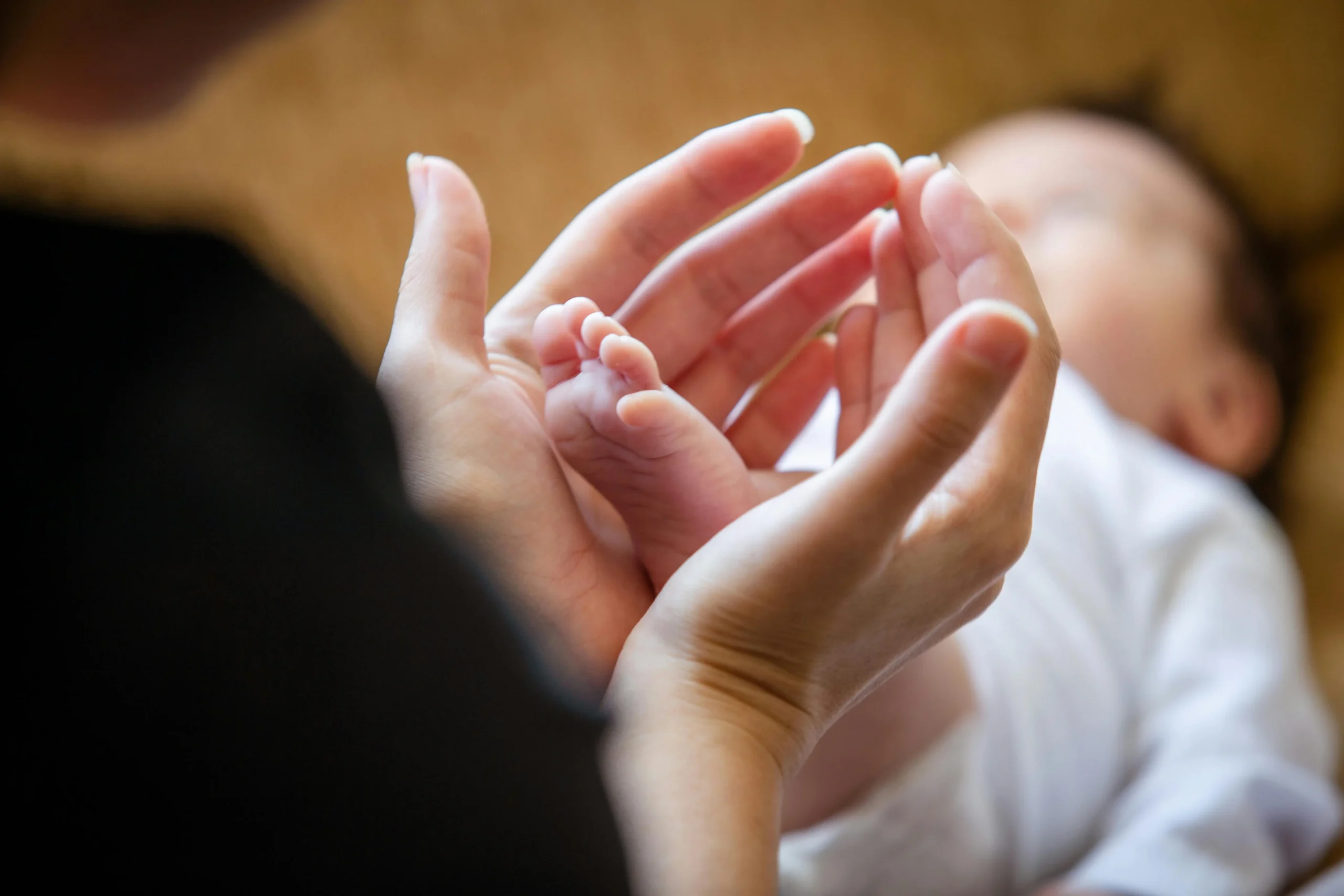 Mains d’adulte enveloppant délicatement le pied d’un nouveau-né – symbole de soin et d’attachement postnatal.
